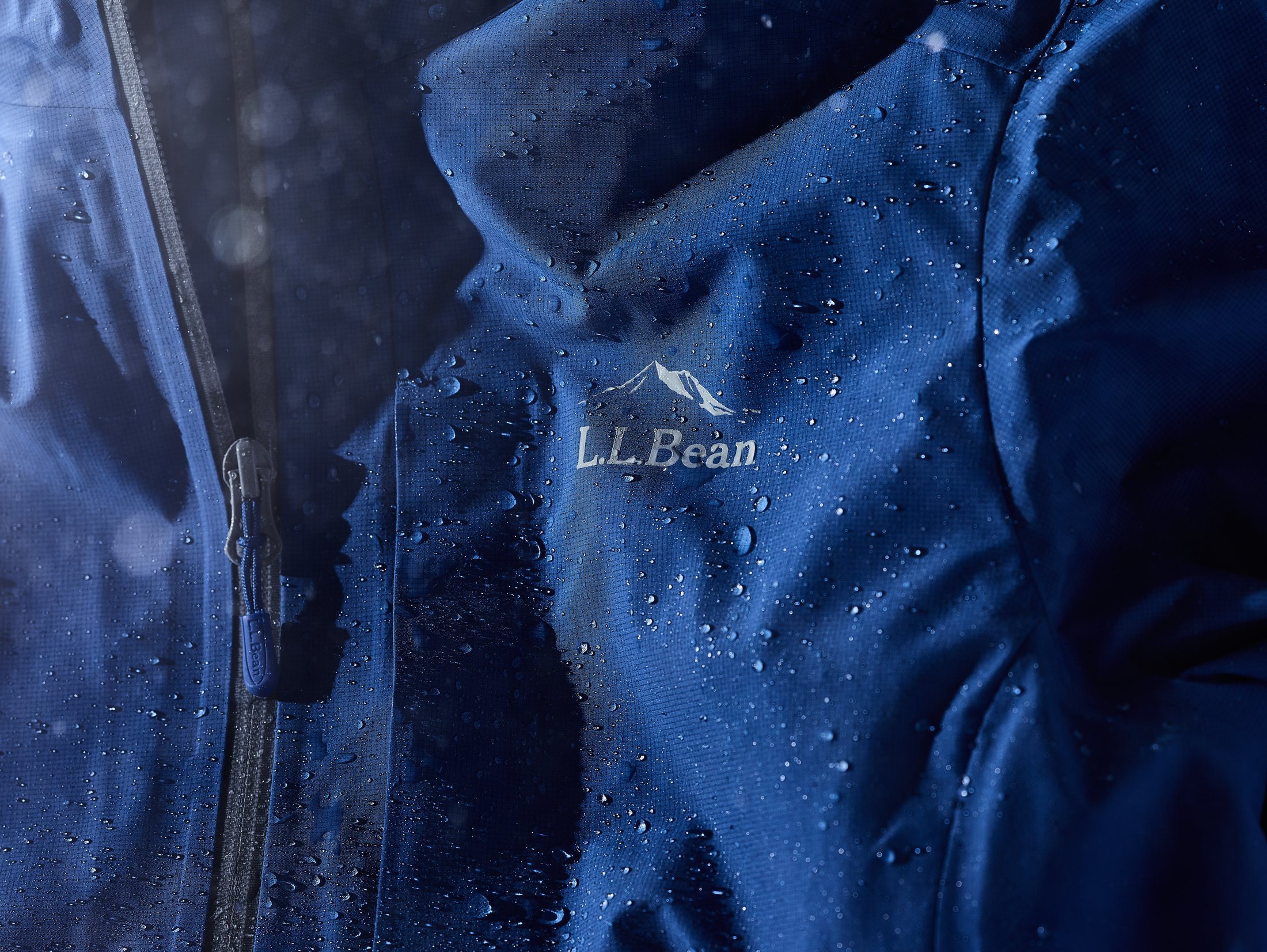 Close-up of the L.L.Bean logo on a navy rain jacket chest, rain droplets on fabric.