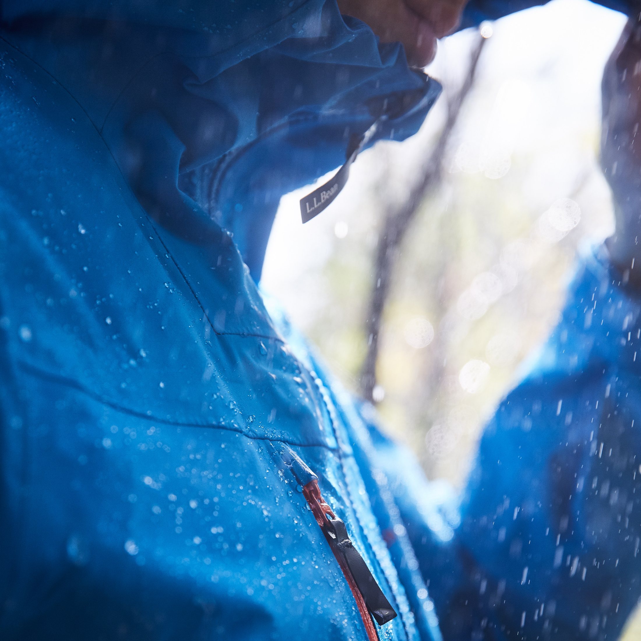Close-up of a hooded navy L.L.Bean rain jacket in the rain, brand tag visible at the collar.