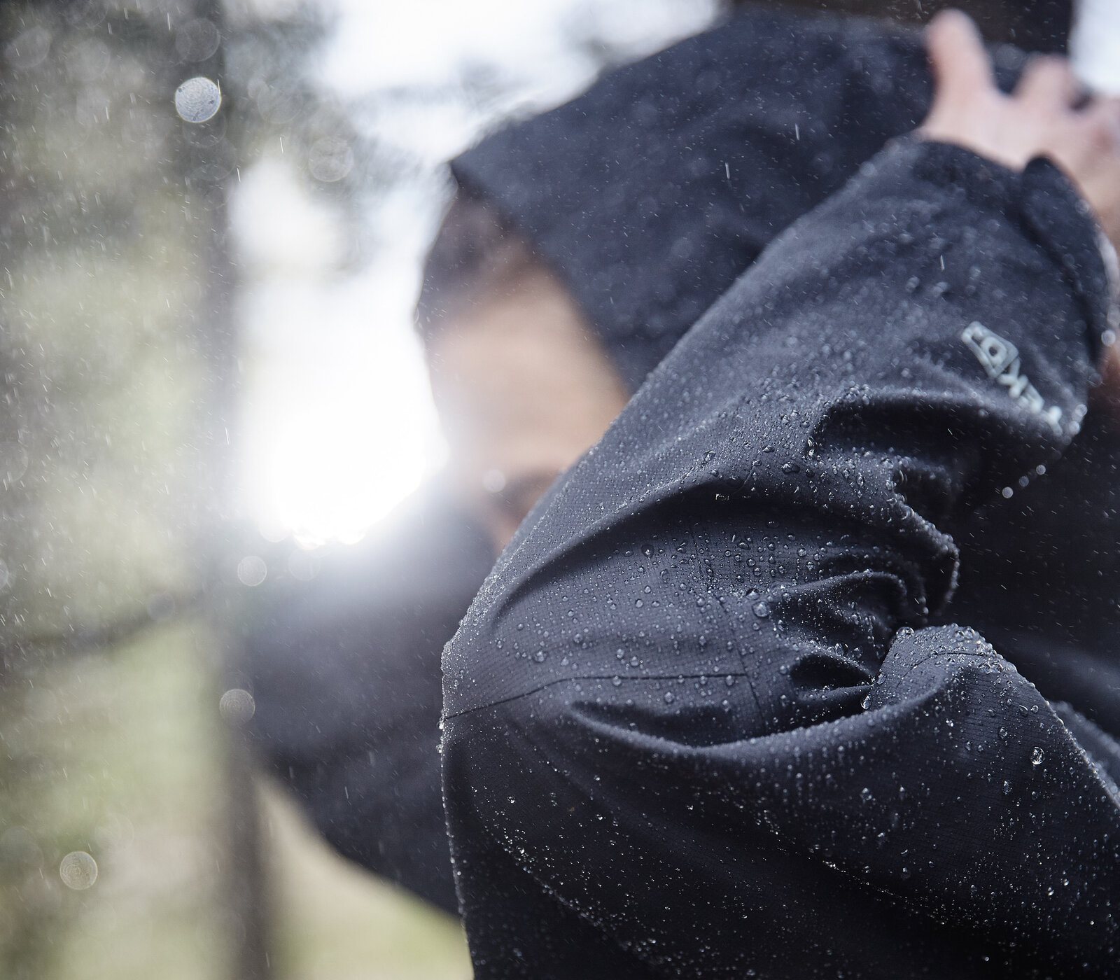 Backlit black rain jacket hood, sun through rain.