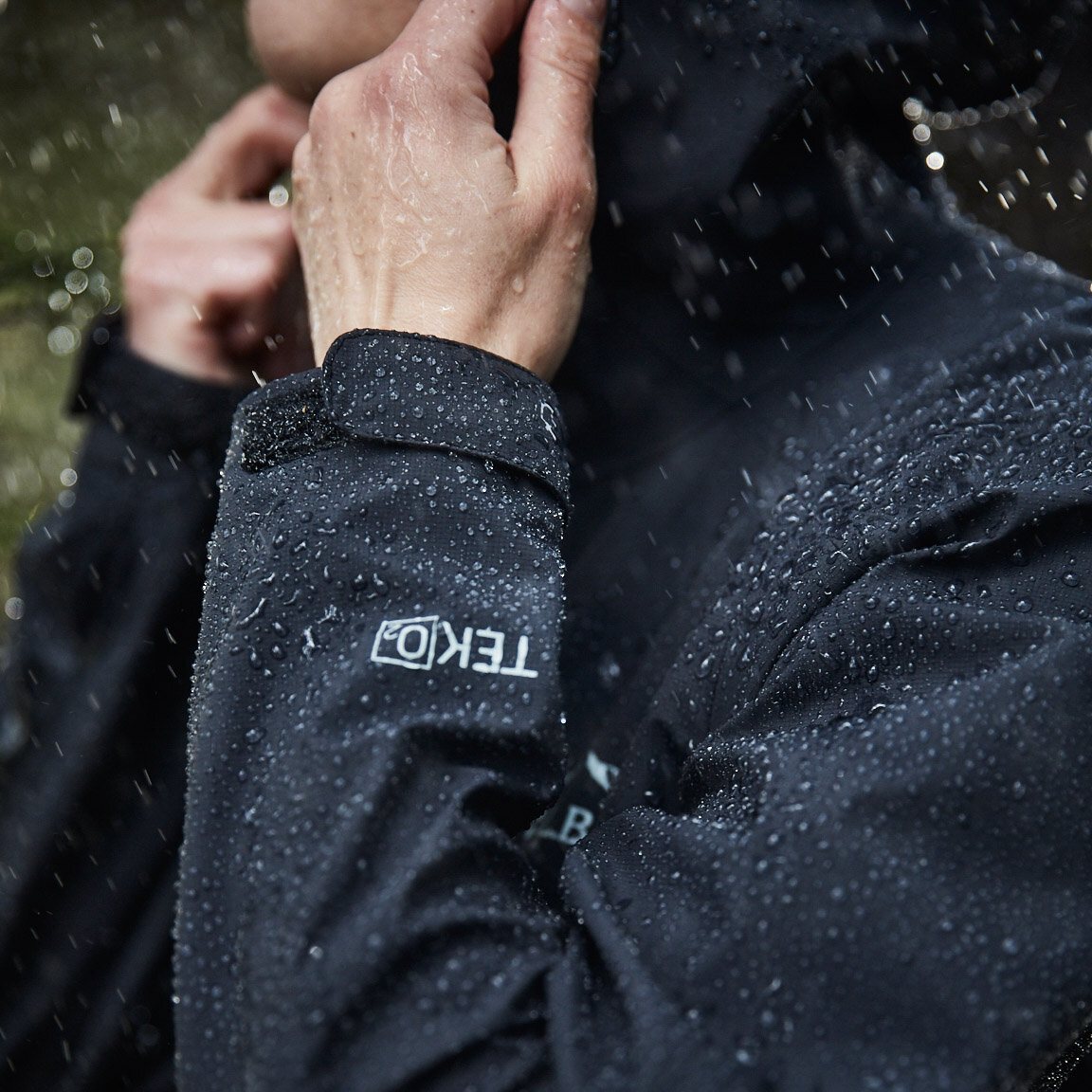 Black jacket cuff with TEK O2 label, hand adjusting hood, rain.