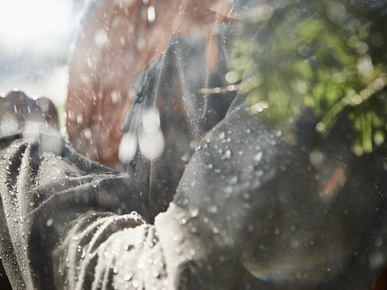 Rain through pine branches, jacket blurred in the background.