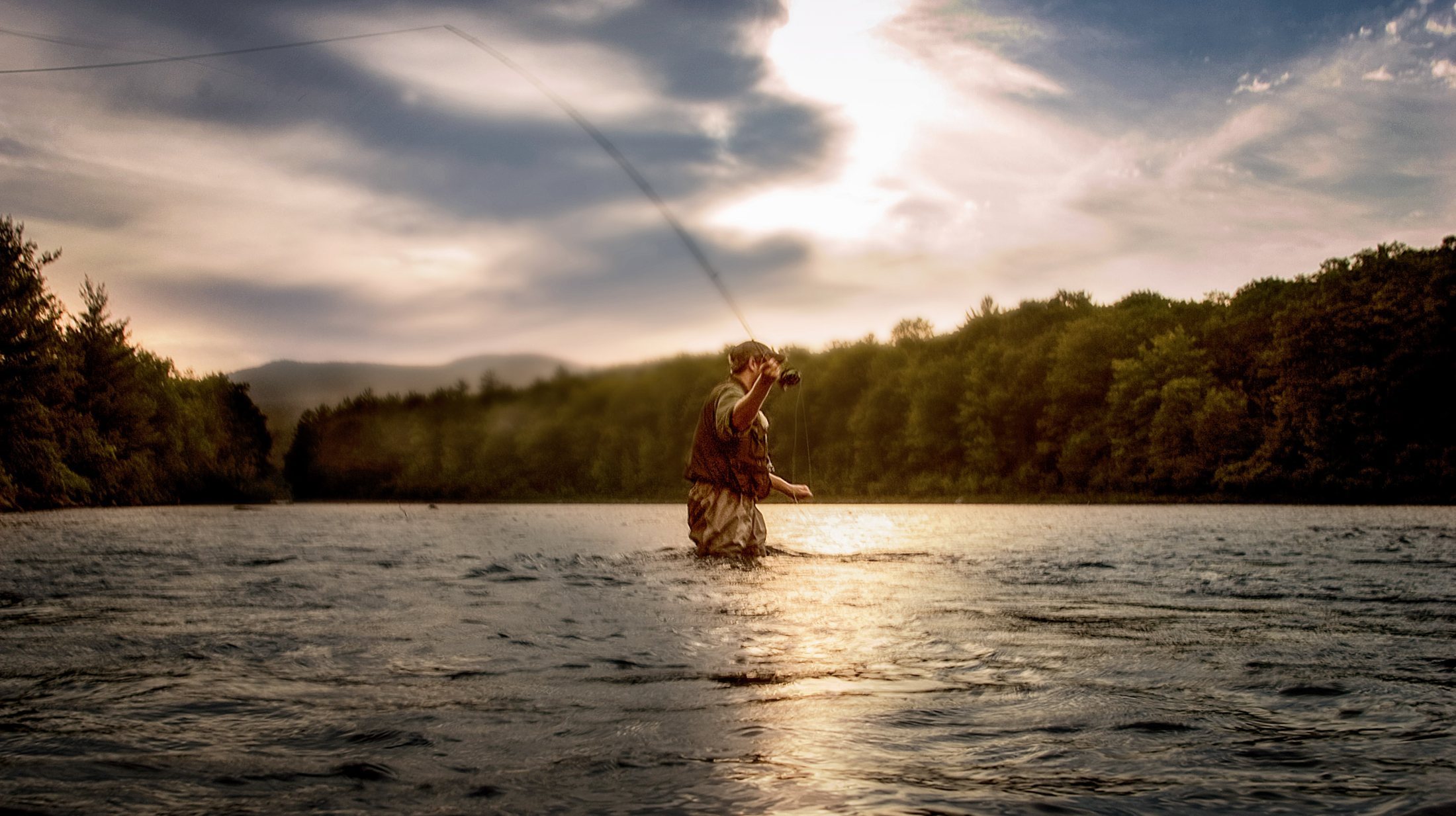 Angler fly fishing at golden hour, backlit against a river at sunset, hunting and fishing lifestyle photography by Rory Scranton.